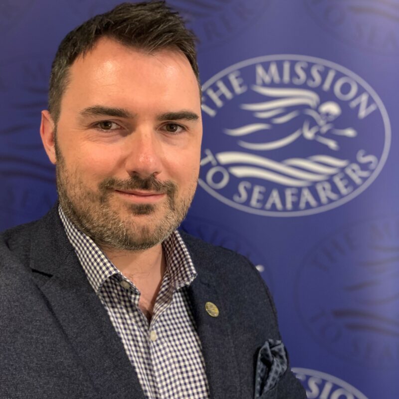 Photo of a man with the Mission to Seafarers logo behind him