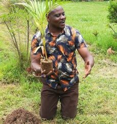 Photo of a man knelt down holding a small plant he is about to plant.