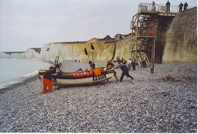 A photo of a group of men on a beach pushing a small lifeboat towards the sea