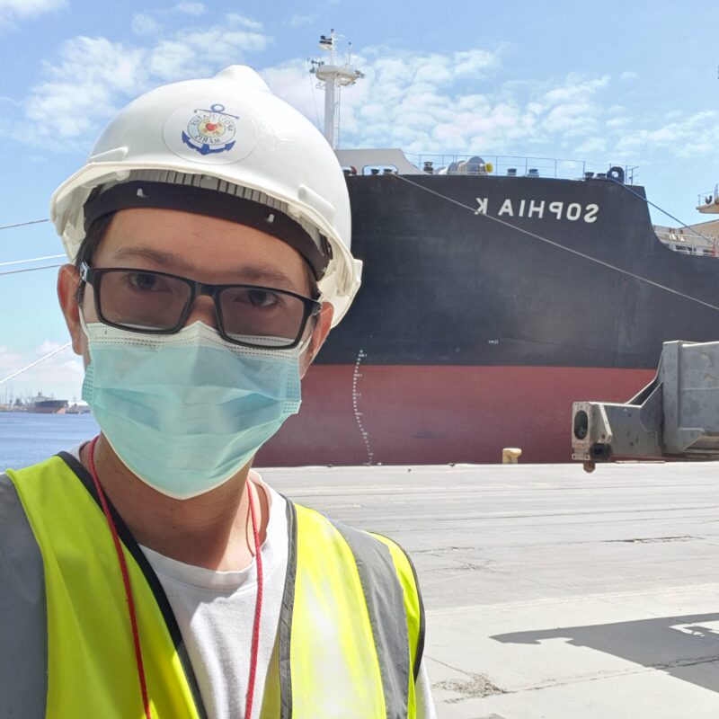 A photo of a man wearing a mask and hard helmet, standing in front of a large ship.