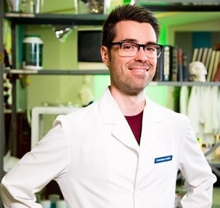A photo of a man smiling wearing glasses and a white lab coat